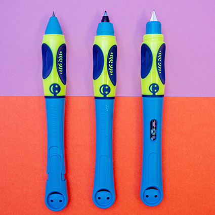 Das Bild ist zweigeteilt. Die obere Hälfte hat einen lavendelfarbenen Untergrund. Die untere Hälfte ist orange. Darauf sind drei blau-grüne Stifte der Griffix-Serie von Pelikan zu sehen. Von links nach rechts: Schreiblernbleistift, Schreiblern-Tintenroller und Schreiblern-Füller. Die Kappen aller Stifte sind abgenommen und man sieht die Spitzen. Foto: Johanna Rundel