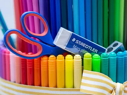 Aus einer Etage einer „Stifte-Torte“ ragen eine blaue Schere, ein weißer Radiergummi und ein Spitzer der Marke Staedtler hervor.