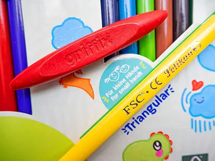 Ein gelber Dreikant-Buntstift von Pelikan liegt neben einer roten griffix-Wachsmalkreide auf der Verpackung der Buntstifte. Foto: Johanna Rundel