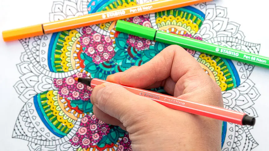 Jemand malt mit neonfarbenen Filzstiften von Stabilo ein Mandala bunt aus.