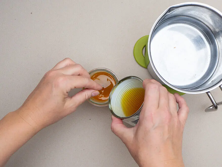 Jemand gießt geschmolzene Bienenwachslinsen von KNORR prandell in ein mit einem Docht präpariertes Marmeladenglas. Foto: Johanna Rundel
