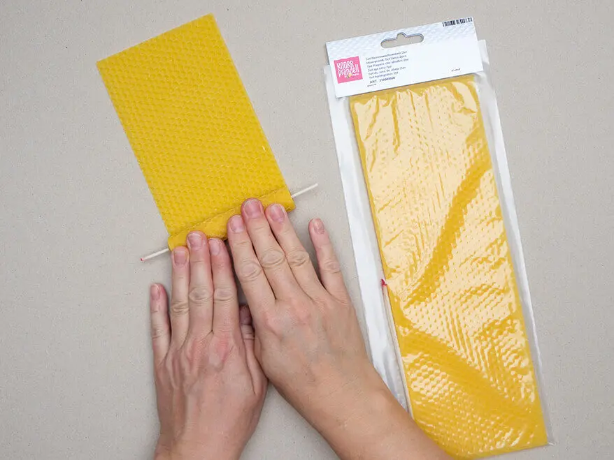 Jemand rollt einen Docht in eine Bienenwachsplatte von KNORR prandell. Eine Packung mit weiteren Platten liegt daneben. Foto: Johanna Rundel