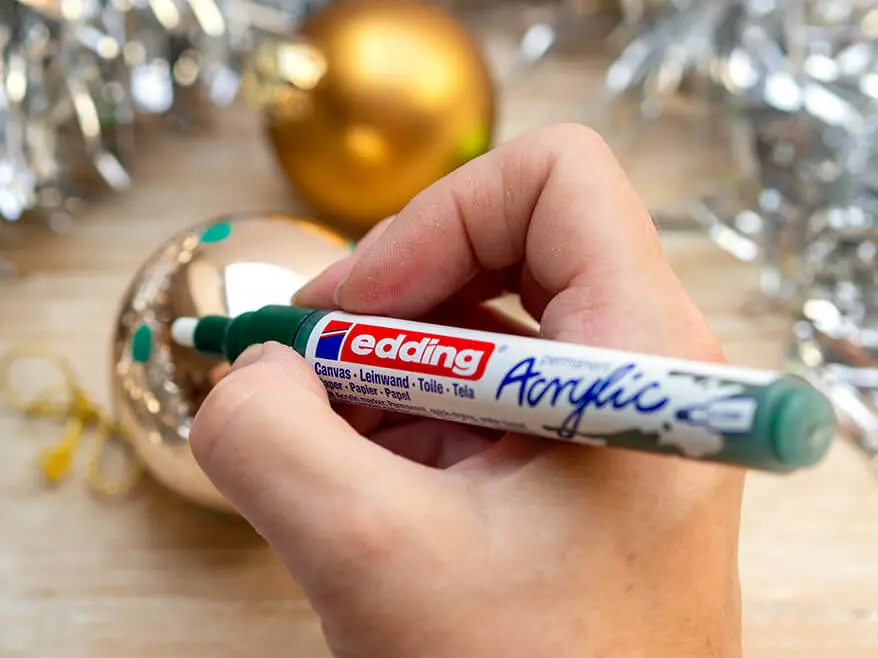 Jemand malt mit einem grünen Acrylmarker von edding Punkte auf eine goldene Christbaumkugel. Foto: Johanna Rundel
