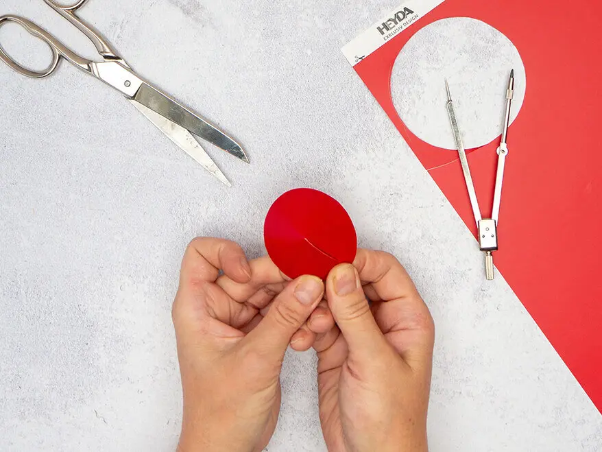 Jemand bastelt aus rotem Karton von HEYDA ein rundes Hütchen. 