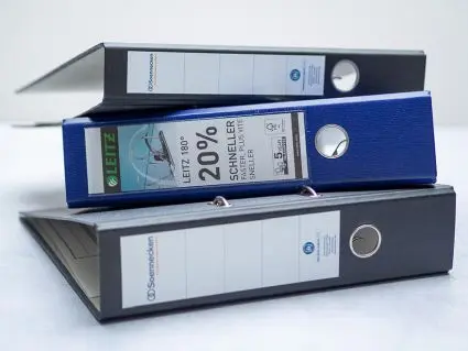 Ein schmaler, ein blauer und ein klassischer Aktenordner liegen übereinandergestapelt auf einem hellen Untergrund. Foto: Johanna Rundel