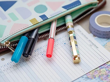Aus einem Mäppchen mit pastellfarbenem Muster von Filofax ragen vier bunte Stifte heraus. Darunter liegt ein Jahresplaner-Einleger. Foto: Johanna Rundel 