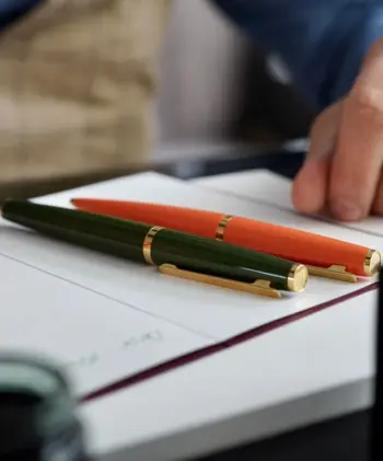 Ein schick gekleideter Büroangestellter sitzt am Schreibtisch. Vor ihm Dokumente auf denen zwei Schreibgeräte von Otto Hutt liegen