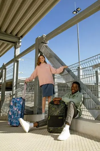 Eine Schülerin und ein Schüler warten nach einer Klassenfahrt mit ihrem Reisegepäck von satch an einer Bahnstation auf ihre Abholung