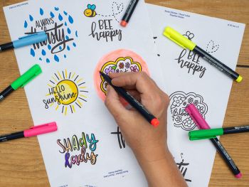 Jemand malt die Letterings auf Avery Zweckform Aufklebern mit Kreativmarkern nach. Foto: Johanna Rundel