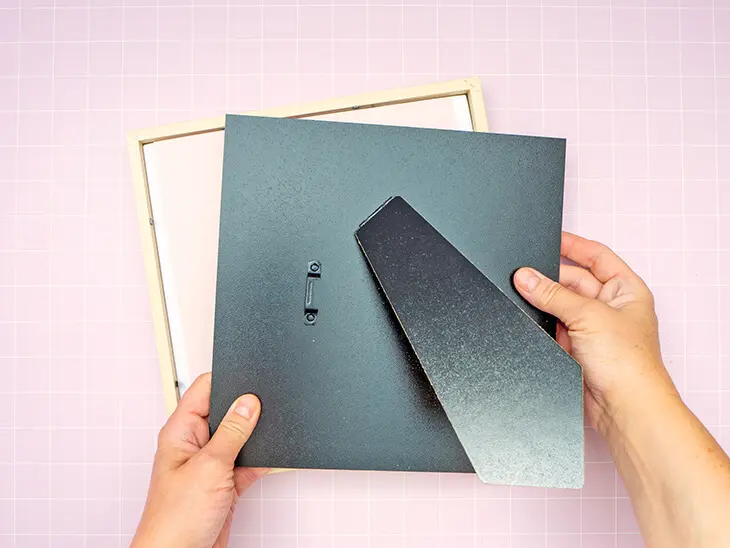 Jemand setzt die schwarze Rückwand in einen quadratischen Bilderrahmen aus Holz ein. Foto: Johanna Rundel