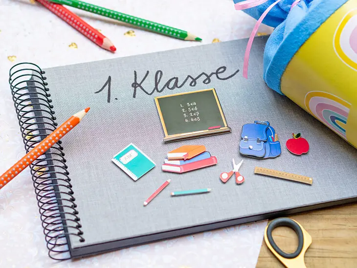 Ein mit passenden Stickern und dem Schriftzug „1. Klasse“ gestaltetes Fotoalbum von Goldbuch liegt zwischen einer Schultüte und Buntstiften auf einem Tisch. Foto: Johanna Rundel