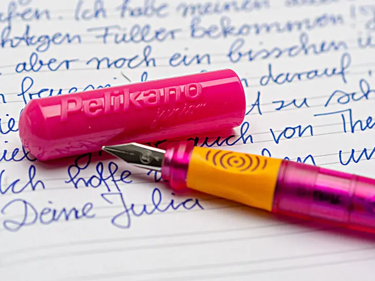 Close-Up eines pink-orangen Pelikano-Füllers von Pelikan der auf einem handgeschriebenen Brief in einem Heft für die dritte Klasse von herlitz liegt. Foto: Johanna Rundel