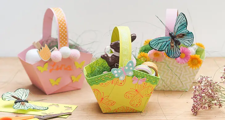 Drei selbstgebastelte Osternester aus Papier von HEYDA, die mit verschiedenen Bastelmaterialien von KNORR prandell verziert wurden, stehen nebeneinander auf einem Holztisch. Foto: Johanna Rundel