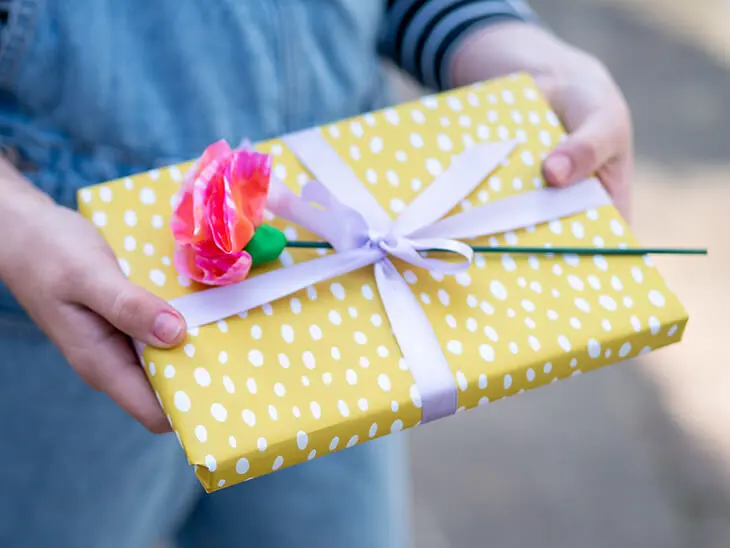 Ein Kind hält ein gelbes Geschenk in den Händen, das mit einer selbstgebastelten Papierblume aus Strohseide von HEYDA verziert wurde. Foto: Johanna Rundel