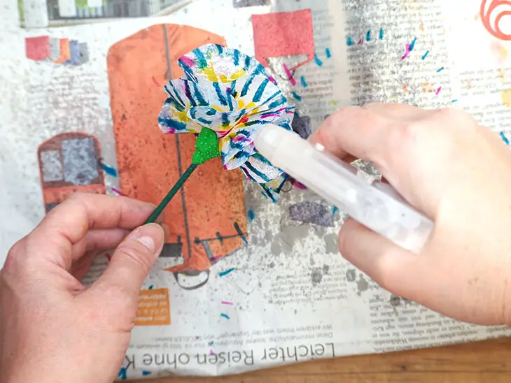 Jemand sprüht eine selbstgebastelte Blume aus Strohseide von HEYDA mit Wasser ein, damit die Farbe verläuft. Foto: Johanna Rundel