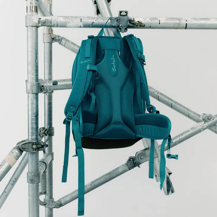 Ein petrolfarbener Schulrucksack von satch hängt an einem Gerüst. Das ergonomische Tragesystem ist zu sehen.