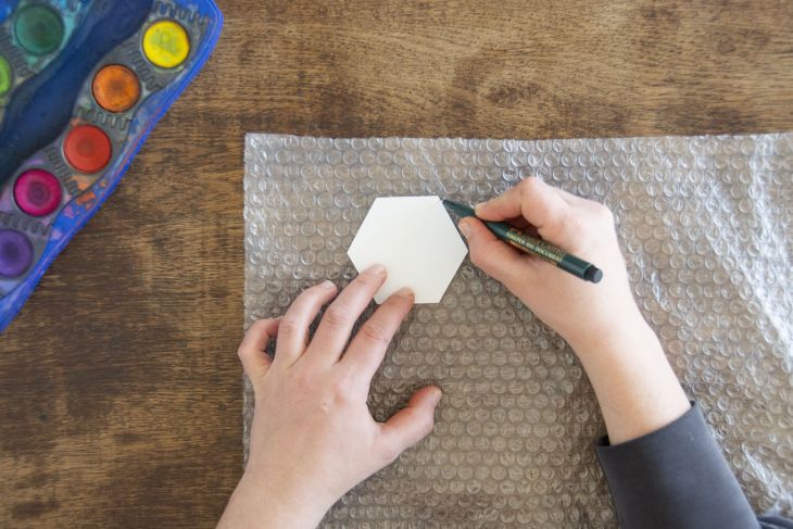 Jemand umrandet eine wabenartige Schablone auf einer Luftpolsterfolie mit einem Fineliner von Faber-Castell.