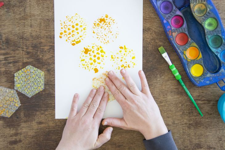 Jemand stempelt Bienenwaben mit Luftpolsterfolie auf ein Papier