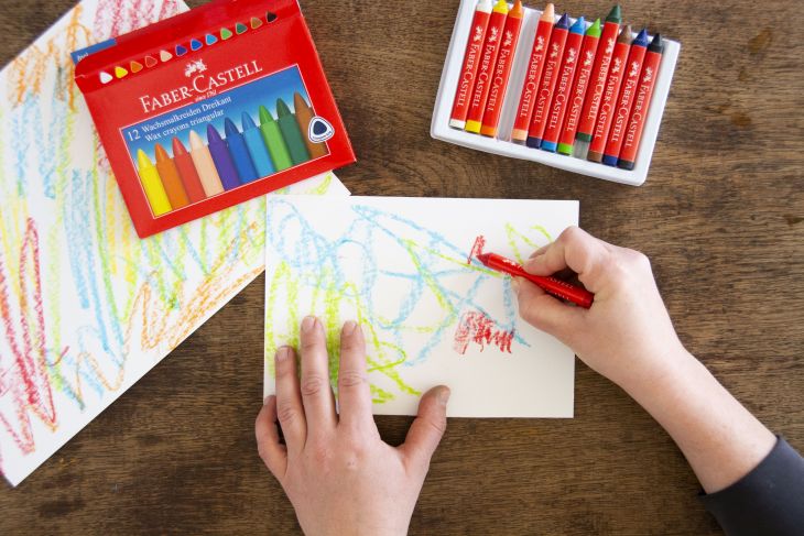 Jemand malt Papier mit Wachsmalkreiden von Faber-Castell bunt an.