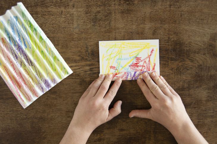 Jemand faltet buntes Papier fächerartig im Zick-Zack.