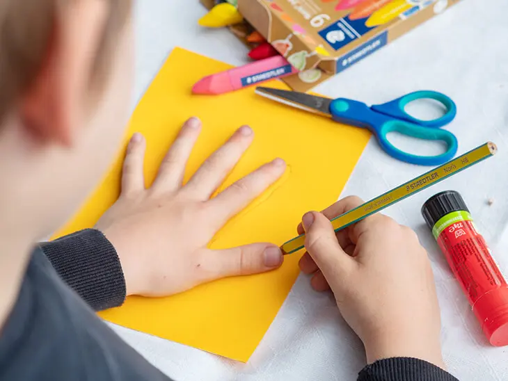 Ein Kindergartenkind zeichnet mit einem Bleistift von STAEDTLER seine Hand auf einem gelben Tonpapier ab. Foto: Johanna Rundel