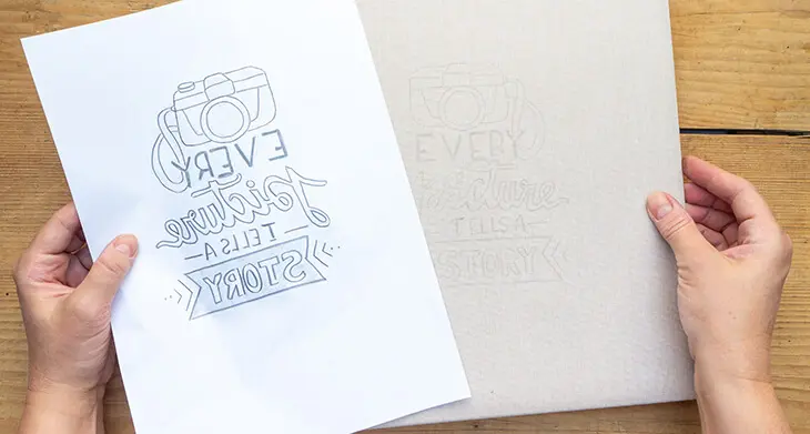 Jemand nimmt eine Bleistiftvorlage eines Letterings von einem Fotoalbum-Cover ab. Der übertragene Abdruck der Vorlage ist darauf zu erkennen. Foto: Johanna Rundel)