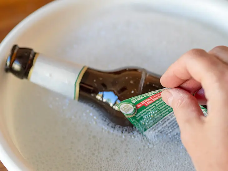 Jemand zieht das Papieretikett einer Bierflasche ab, die in einer Schüssel mit Seifenwasser liegt. Foto: Johanna Rundel