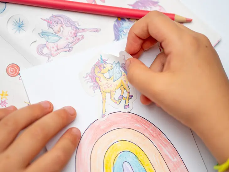 Kinderhände kleben einen Einhornaufkleber von Coppenrath auf eine Geburtstagseinladung. Foto: Johanna Rundel