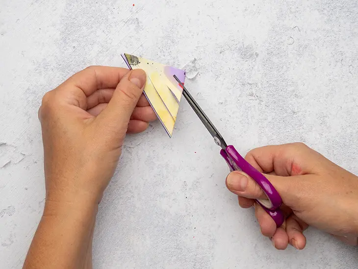 Jemand schneidet mit einer Pelikan-Schere Schlitze in ein buntes Papierdreieck. Foto: Johanna Rundel