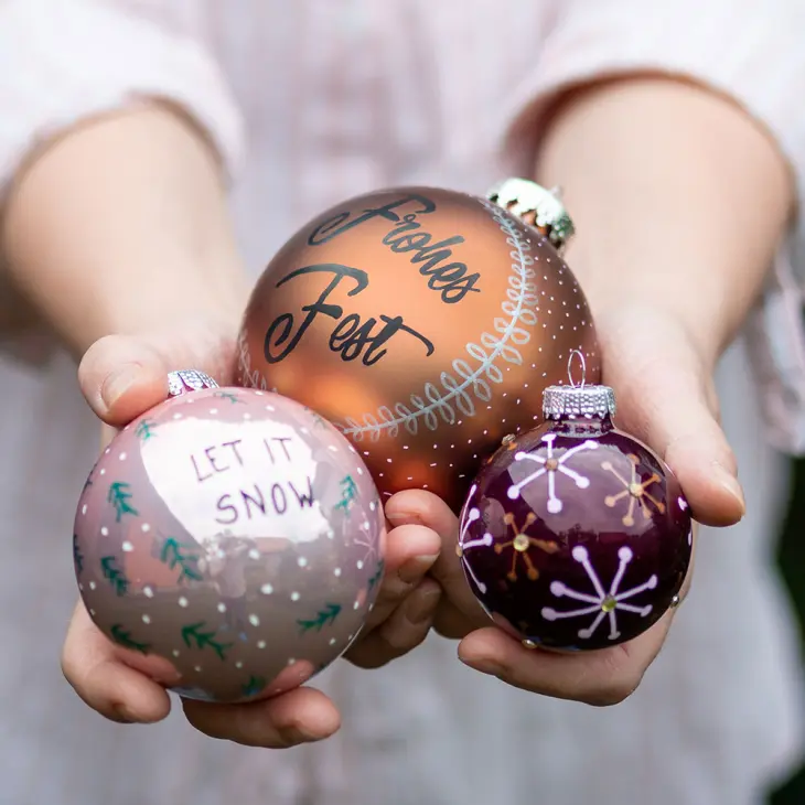 Eine Frau hält drei selbst bemalte Weihnachtskugeln in den Händen