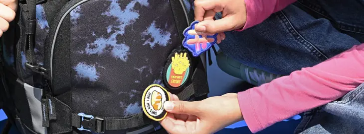 Eine Hand heftet einen COLOUR UP-Patch an einen Schulrucksack von coocazoo.