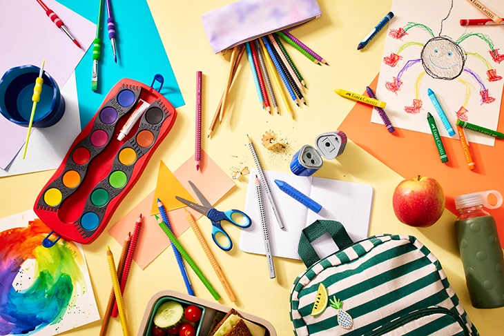Auf bunten Papieren liegen diverse Schulmaterialen von Faber-Castell verstreut.
