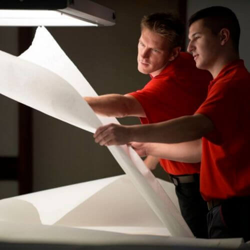 Zwei Mitarbeiter prüfen einen großen Bogen Papier.