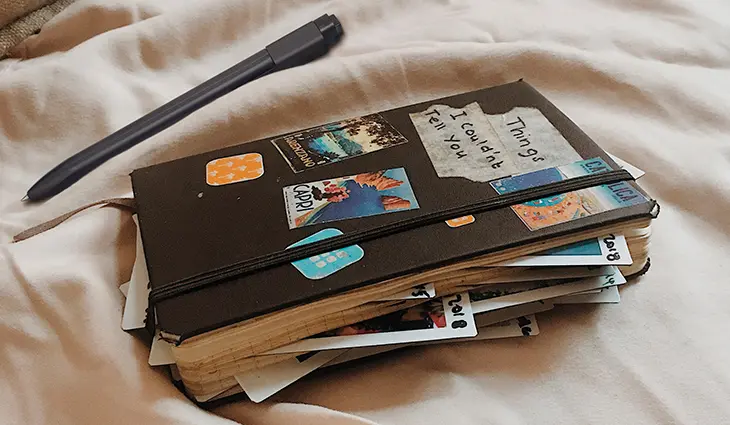 Auf einem Tuch liegt ein schwarzes Notizbuch von Moleskine, das mit Foto vollgestopft und beklebt ist.