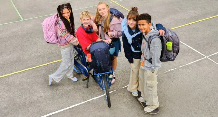 Mehrere Kinder mit satch Rucksäcken auf dem Rücken springen vor einem Scheinwerfer eines Filmsets.