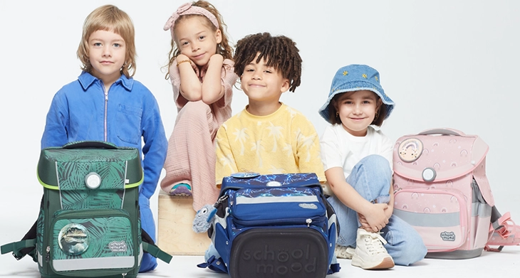 Vier Kinder blicken in die Kamera. Vor ihnen stehen 3 Schulranzen von School-Mood