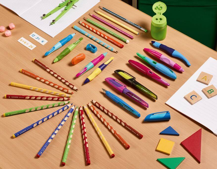 Auf einem Tisch liegen diverse bunte Stifte, Radiergummis und Spitzer aus dem Sortiment von Stabilo.