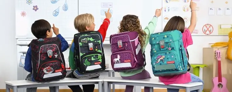 Kinder sitzen im Klassenzimmer mit Schulranzen auf dem Rücken. Text auf dem Bild "Schulranzen-Trends: Was diese Saison angesagt ist".