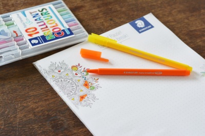 Auf einem Block mit einem Mandala liegen 2 Filzstifte der Marke Staedtler. Die Packung mit den restlichen Stiften liegt neben dem Block.