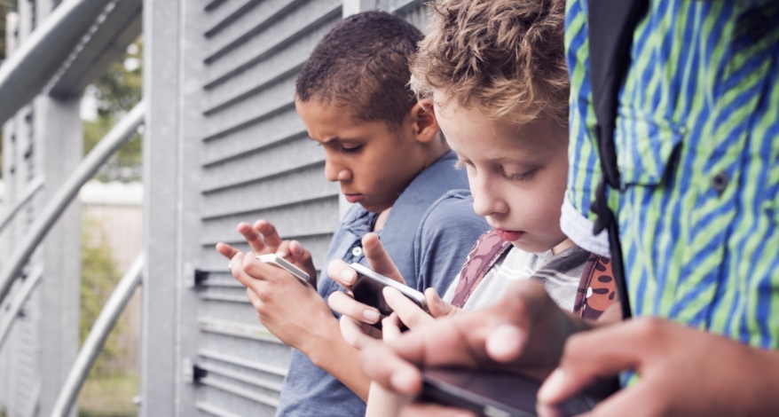 Drei Kinder lehnen an einer Wand, jedes schaut auf sein Smartphone und tippt darauf.