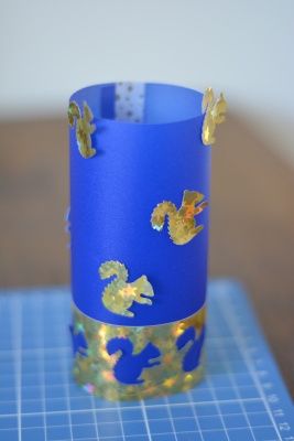 Ein fertiges selbstgebasteltes Windlicht aus blauem Transparentpapier mit goldenen Eichhörnchen.