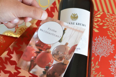 Hand klebt Etikett mit Weihnachtsgrüßen auf eine Weinflasche.