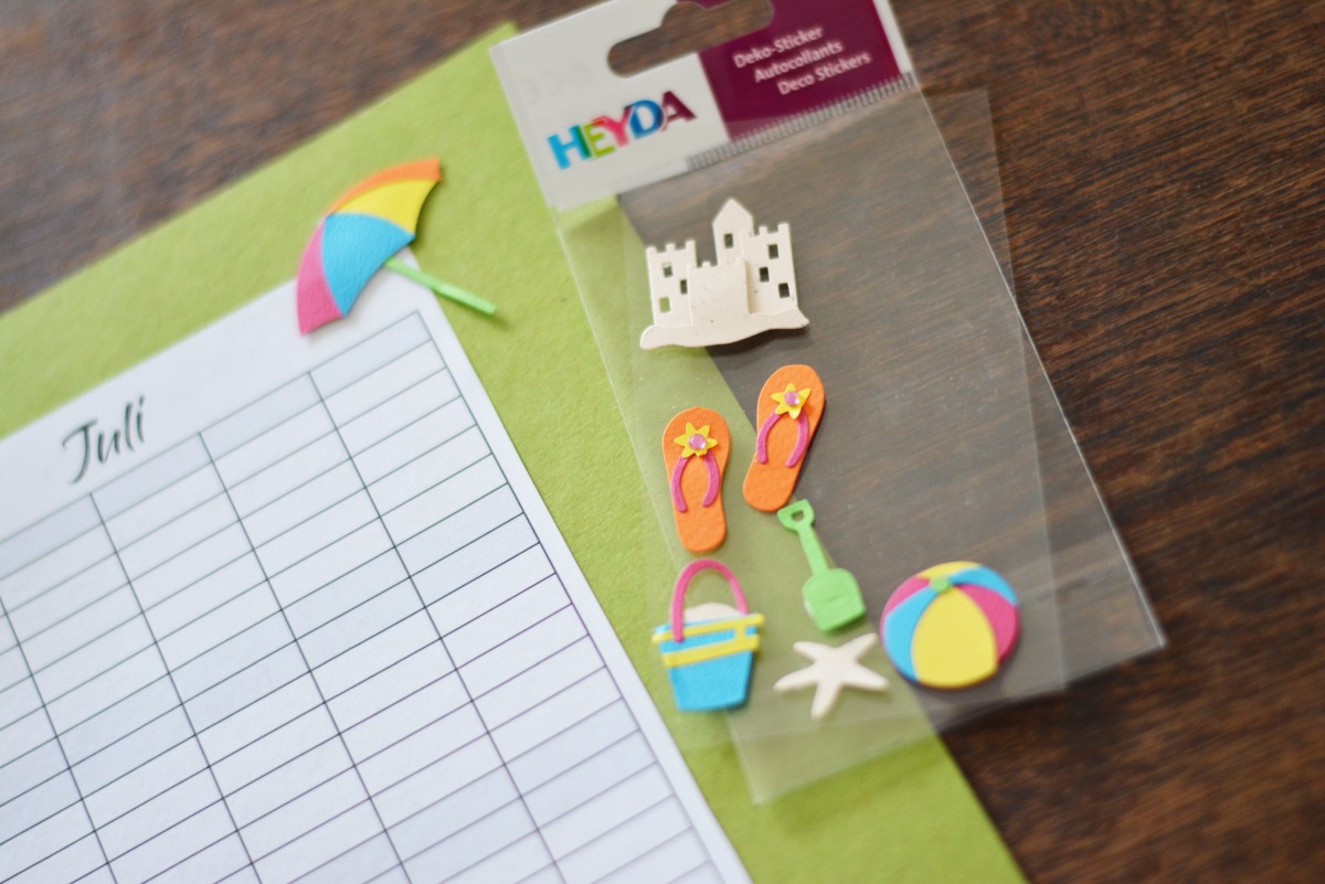 Sommer-Sticker wie Flip-Flops und Ball von Heyda neben Planer auf grünem Karton.