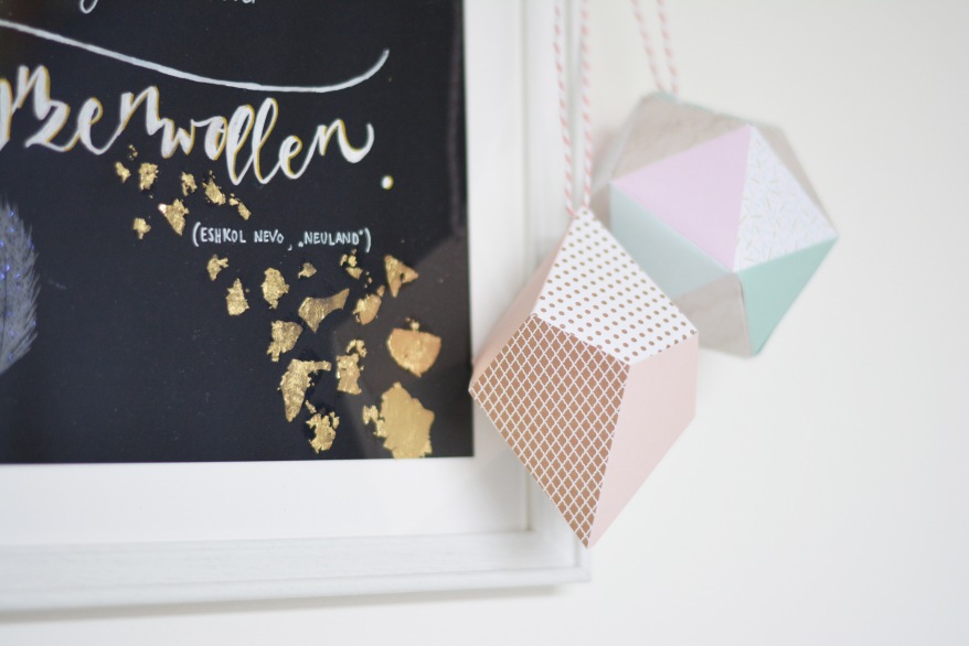 Detailfoto von Lettering mit Goldfolie und zwei bunten Hängedekos aus Papier. 