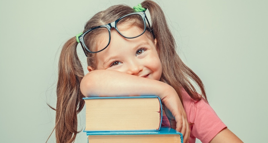 Lächelndes Mädchen mit Brille lehnt sich auf einen Stapel Bücher.
