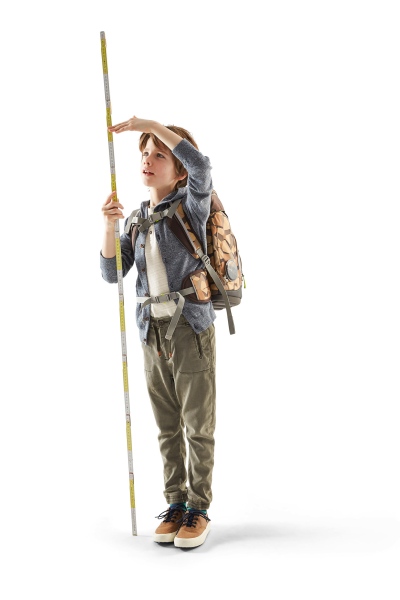 Junge mit Schulrucksack misst seine Größe mit einem Zollstock