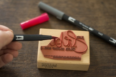 Roter Brushpen wird zum Einfärben eines Holzstempels mit Schriftzug genutzt.