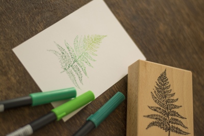Grüner Farn auf Karte gestempelt, daneben Stempelblock und Brushpens.