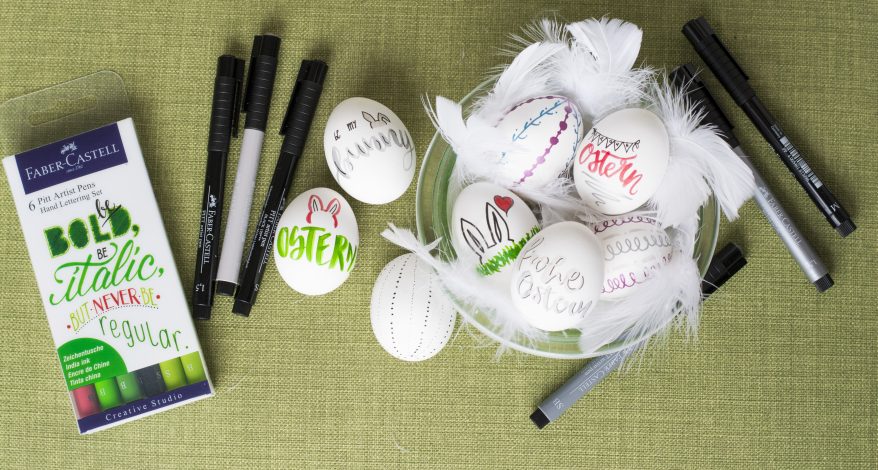 Beletterte Ostereier, Stifte und Verpackung auf grünem Stoff