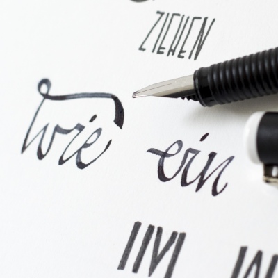 Closeup eines beletterten Papiers auf dem eine Kalliegrafiefeder zu sehen ist. 